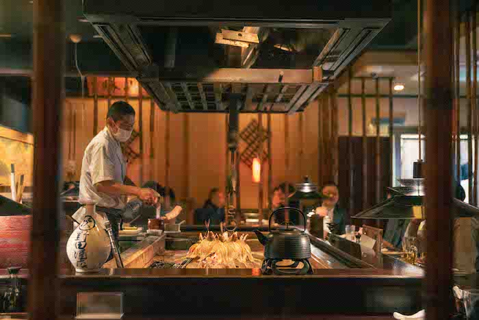 A chef checks on grilling fish at a robatayaki eatery