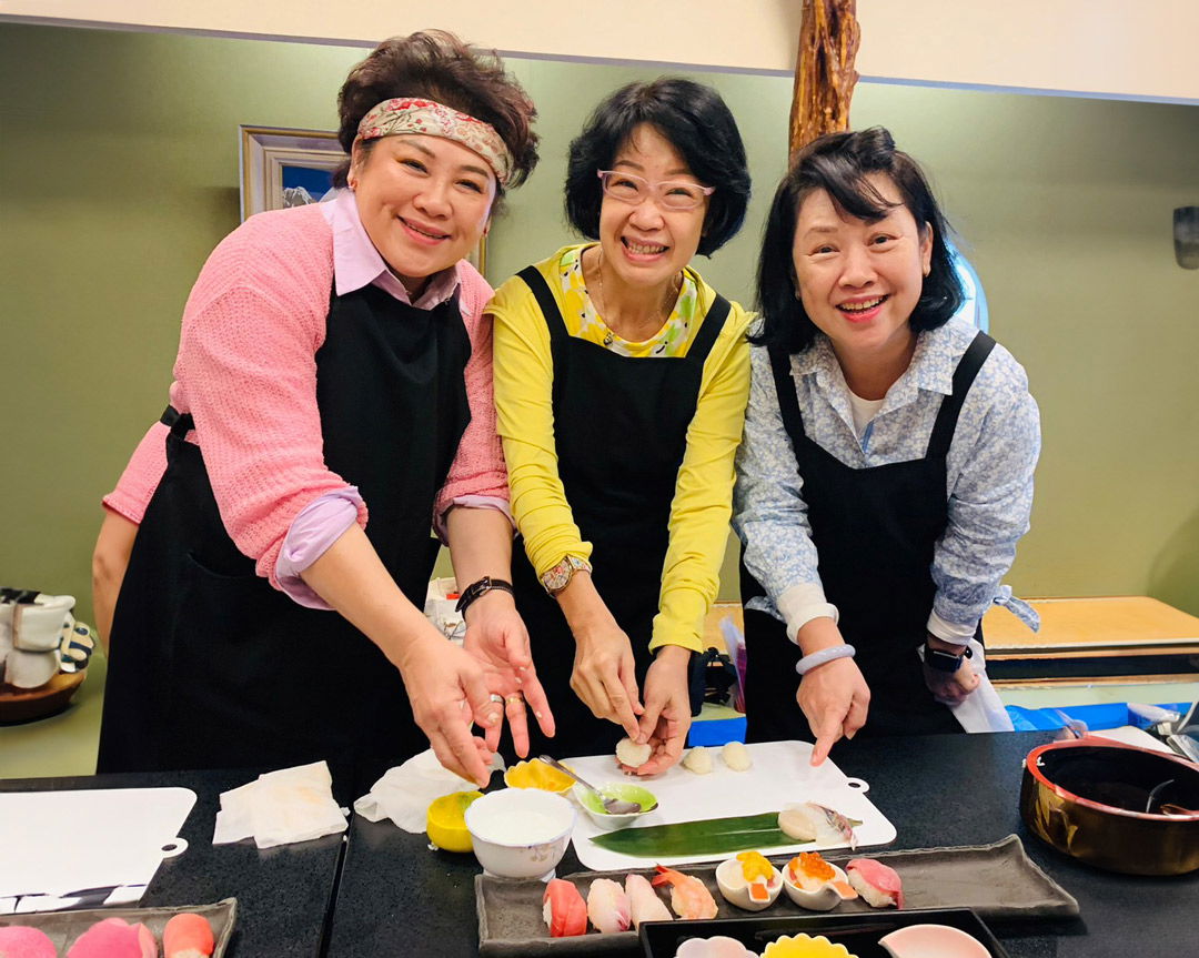 Three guests smiling at the camera, making sushi in a Niigata cooking class.