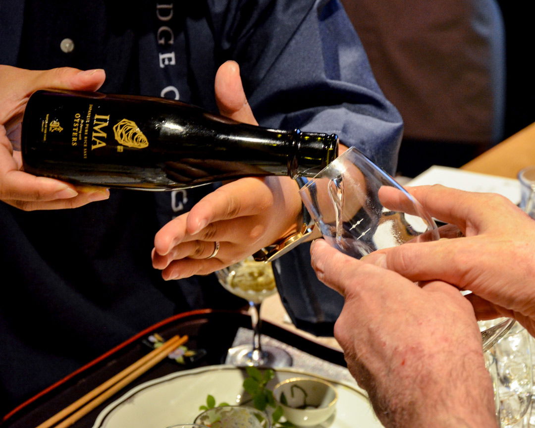 A host pouring another glass of sake for a waiting guest.