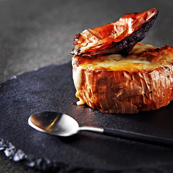 Gourmet dish of roasted onions on slate plate with spoon