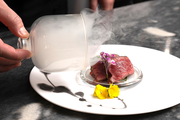 Gourmet smoked beef dish with floral garnish on elegant white plate