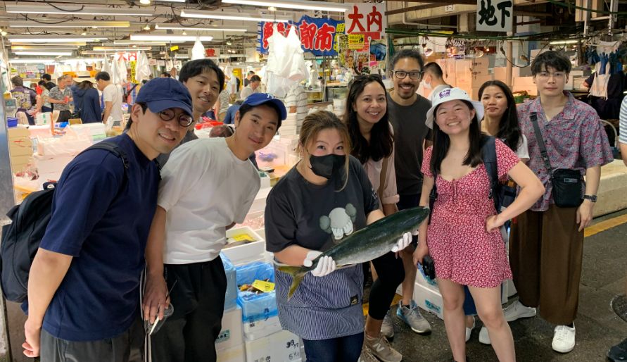 A shopkeeper showing a fresh fish with tour participants at the Triangle Market in Otaru