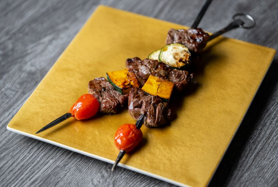 Skewers of luxury beef and vegetables overlapping each other, resting on a gold-colored serving plate.