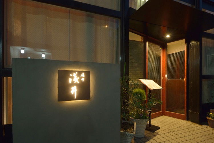 The modern entrance to Azabu Asai, with the restaurant's sign underlit with a warm glow.