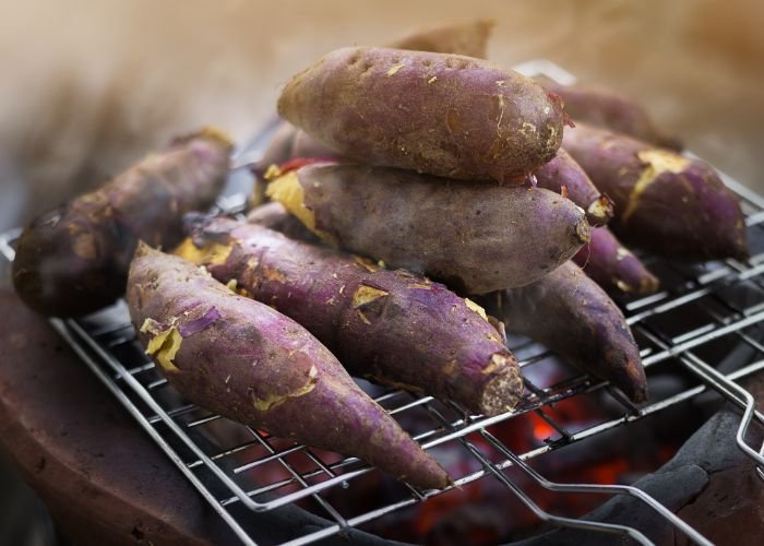 Half a dozen Japanese sweet potatoes roasting on a grill.