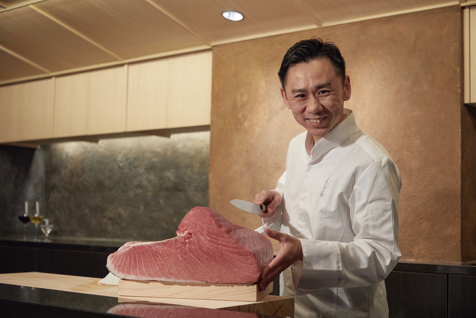 The smiling, expert chef of Ajuta, showing a premium cut of fish to the camera.