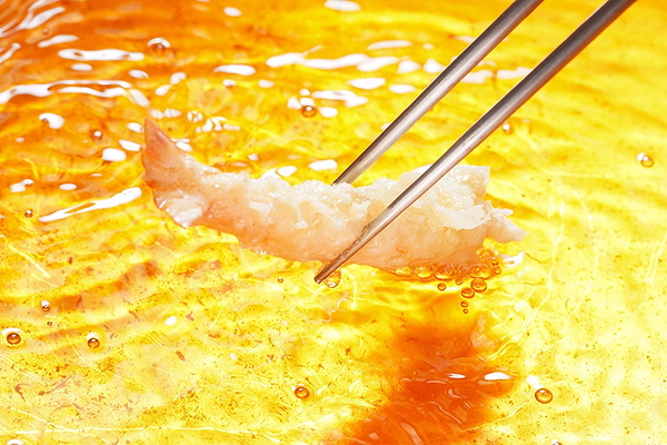 Chopsticks holding shrimp in hot frying oil