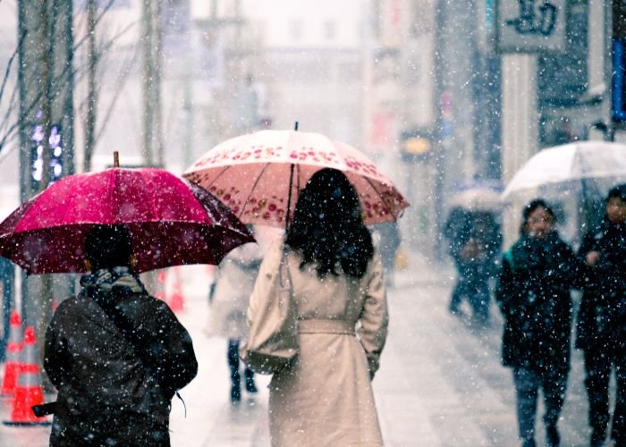 A photo of a woman walking while it's snowing in a Japanese city