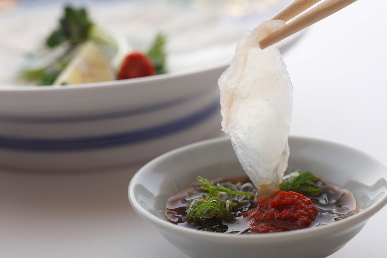 A slice of fugu sashimi being dipped into a sauce at Torafugu-tei Ginza.