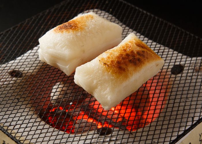 Two pieces of mochi on a charcoal grill