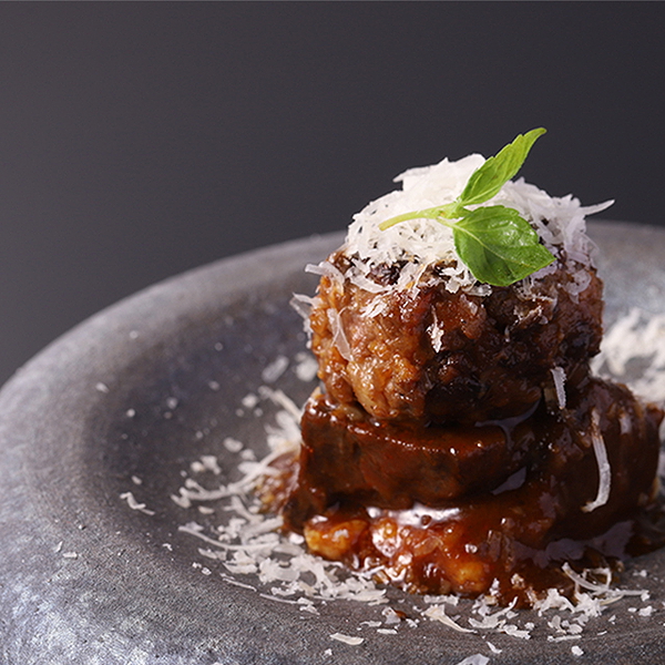 Gourmet meatball dish garnished with cheese and basil on a dark plate