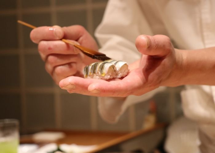 A sushi chef brushes soy sauce on a piece of nigiri sushi