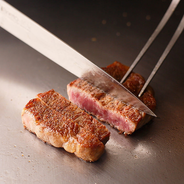 Juicy steak being expertly sliced on a restaurant grill.