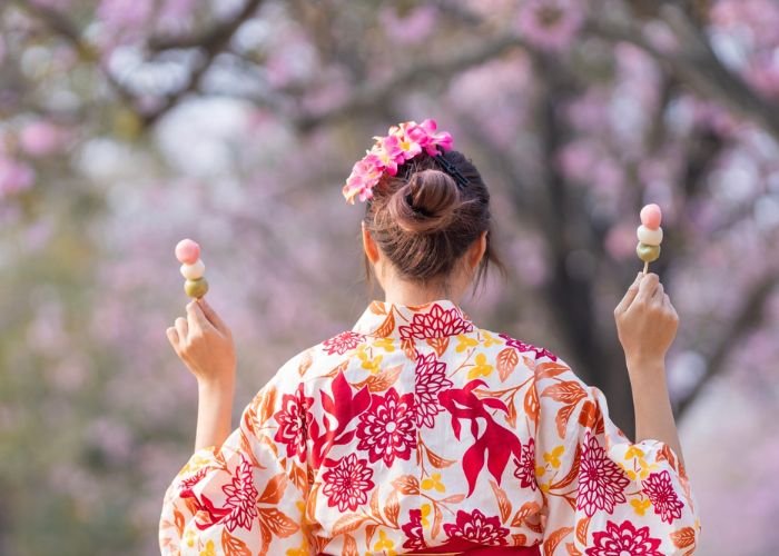 A Japanese woman wearing a kimono is eating dango under cherry blossom trees in Tokyo