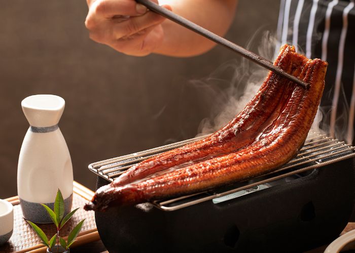 A large slab of unagi eel being flipped on a grill, like it might be at Unagi Hashimoto.