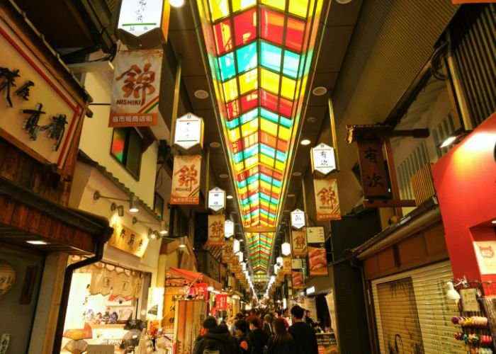 An interior shot of Kyoto's Nishiki Market, showing a multi-colored skylight and many shops.