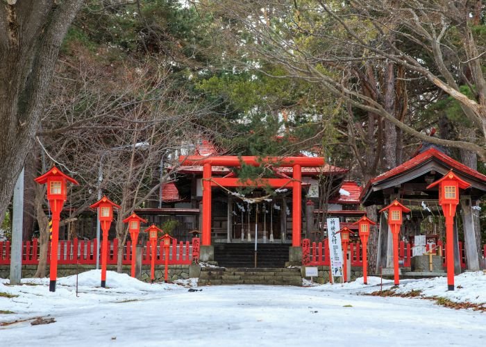 Sapporo's Fushimi Inari Shrine during winter. The bright red torii gate and lanterns contrast against the snow.