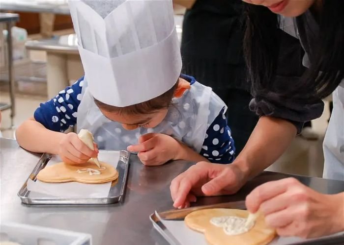 An adult helps a child decorate Shiroi Koibito cookies in a byFood food experience.
