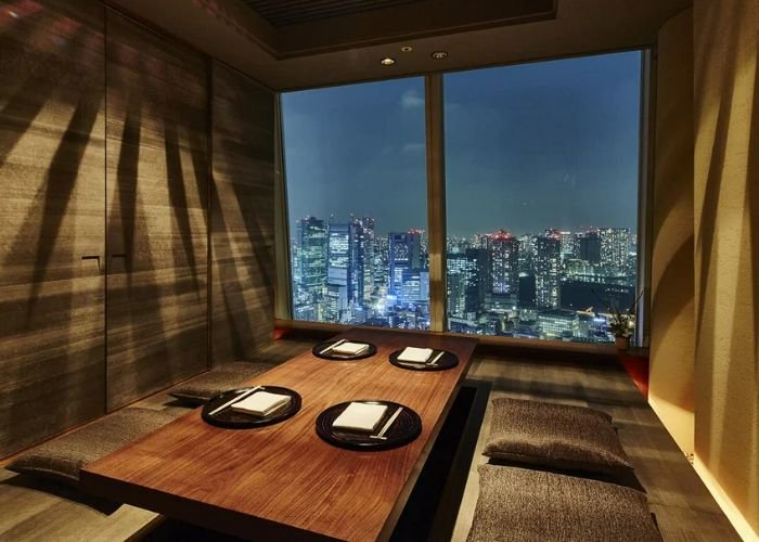 A private room in XEX ATAGO GREEN HILLS, overlooking the Tokyo skyline at night.