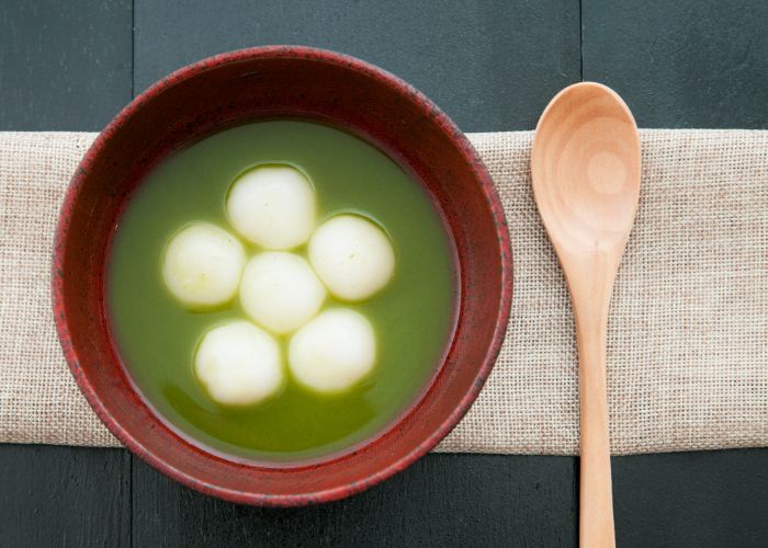 A top-down shot of a matcha zenzai in a red bowl. Six chewy mochi float in the sweet matcha dessert.