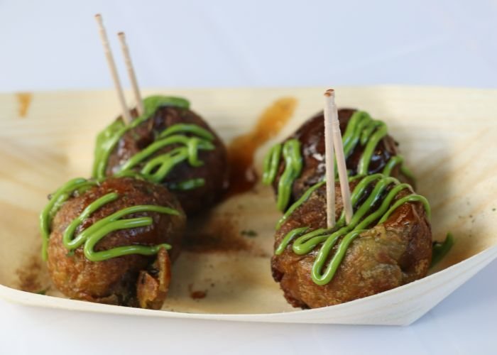 Four takoyaki in a bamboo tray, topped with a dark green matcha sauce.