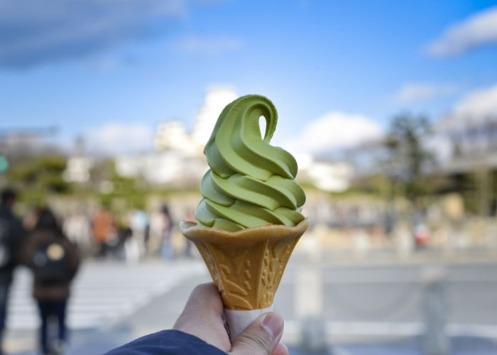 A person holding a matcha ice cream in a wafer cone up in front of them, with the background out of focus.