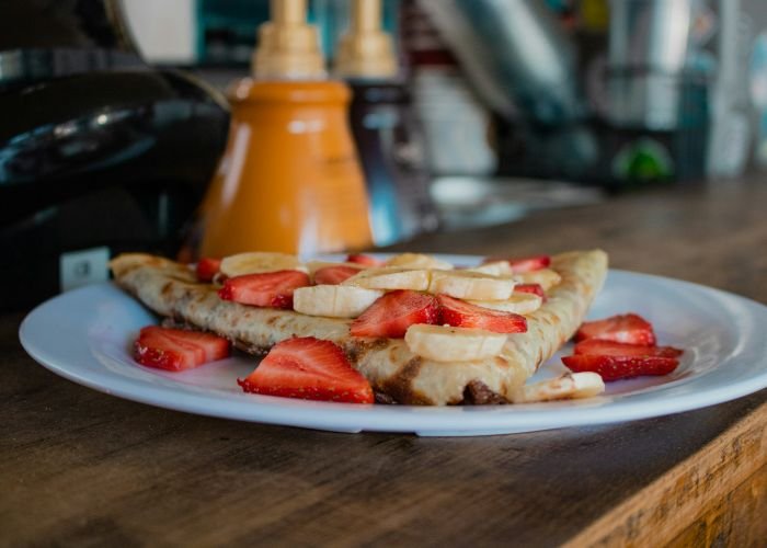 Sliced strawberries and bananas on a crepe, served and waiting on a wooden counter.