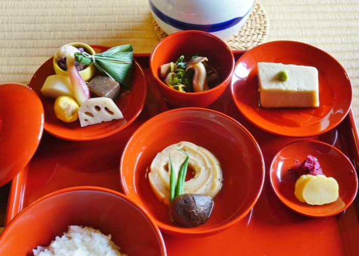 A top-down shot of a shojin ryori teishoku, featuring a range of tofu and vegetable dishes on red lacquerware.