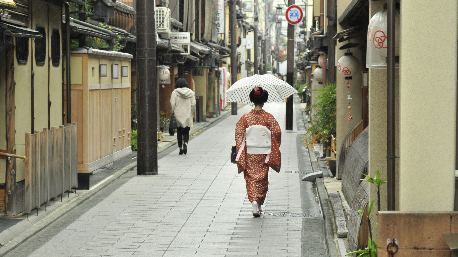 Woman in kimono walking down traditional Japanese street with umbrella
