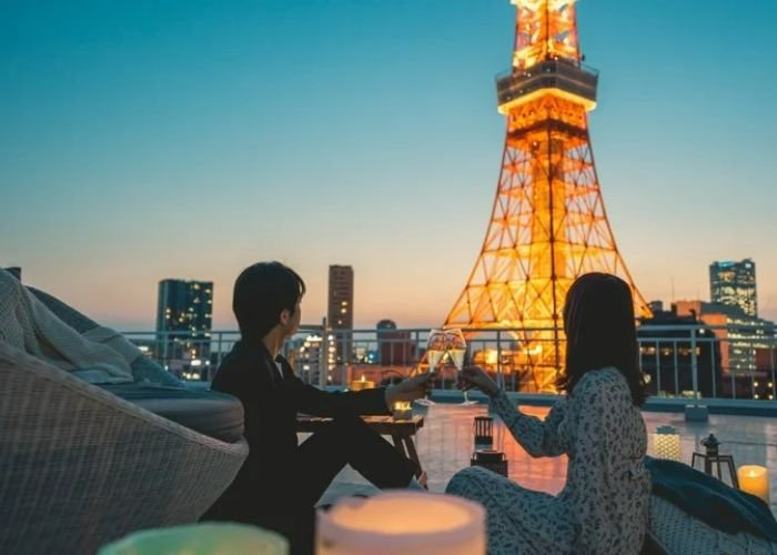 A couple clinking glasses from the roof of Prince Hotel, looking up at Tokyo Tower.