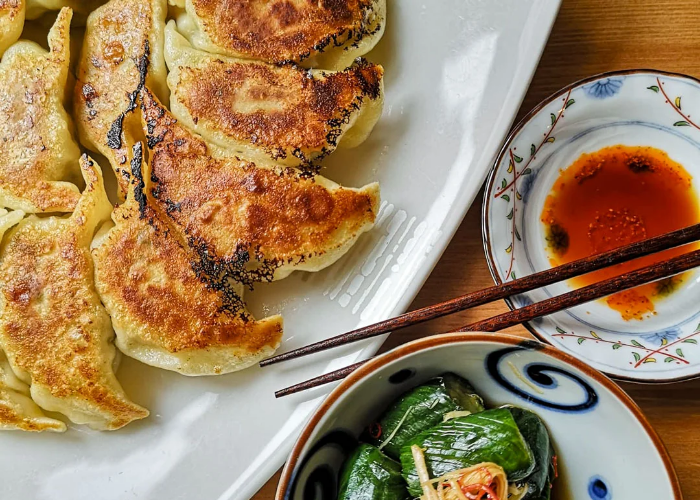 Close-up of fresh gyoza, a side dish, sauce, and chopsticks.