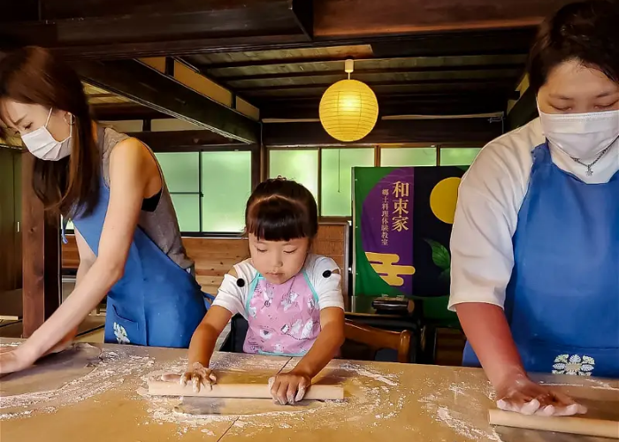 Two adults and one child in a traditional Japanese building, rolling out fresh udon.