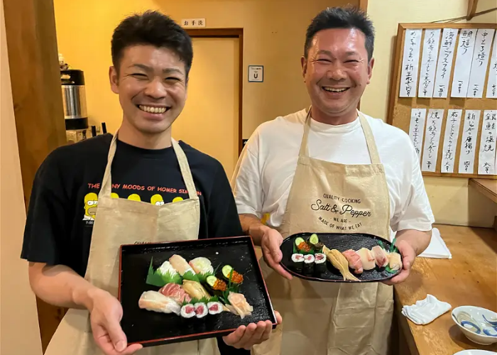 Two men holding their handmade sushi towards the camera, smiling.