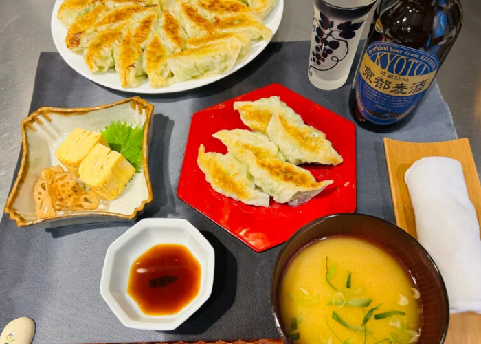 A table is covered in gyoza, rolled omelet, miso soup and beer.