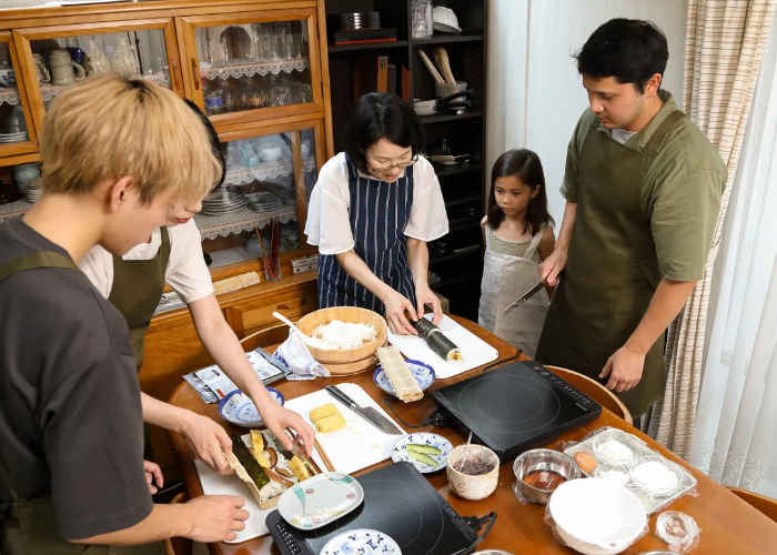 A family listens intently to their Japanese instructor, teaching them how to make Japanese home cooking.