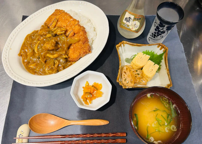 A table is covered in katsu curry, miso soup, rolled omelet, and sake.