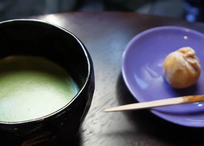 A cup of matcha and a Japanese sweet on a purple plate.