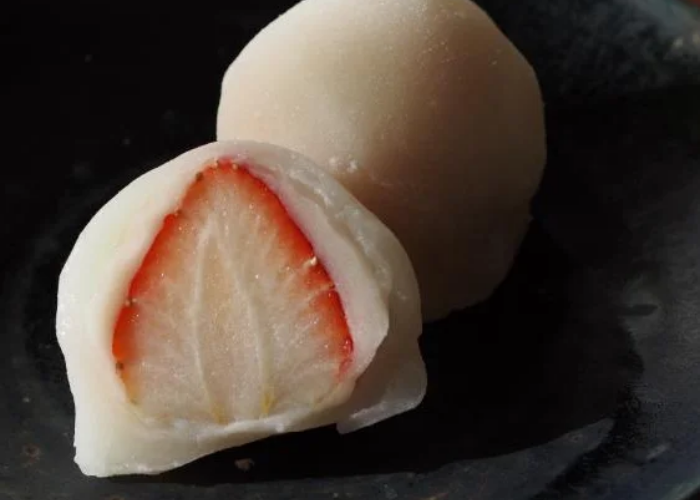 A daifuku cut in half, revealing a fresh strawberry inside a mochi exterior.