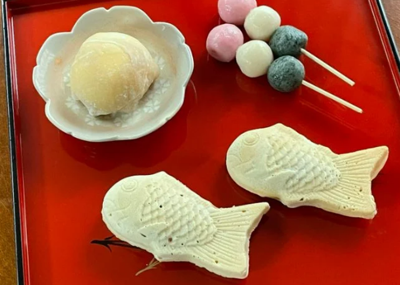 A red tray with a selection of Japanese sweets, including mochi, taiyaki, and dango.
