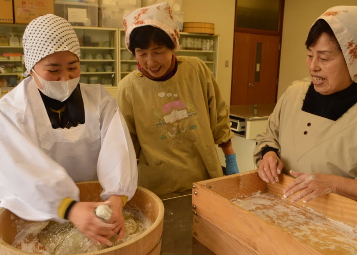 Two Japanese ladies show a guest how to make mochi.