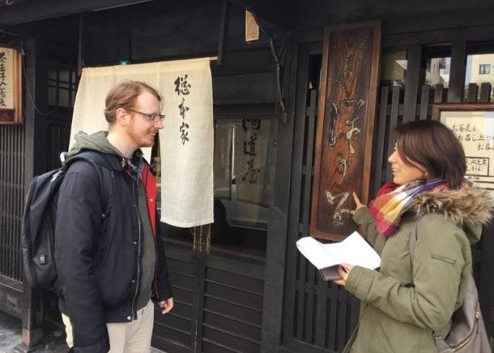 A tour guide talks to a guest outside a traditional building in Kyoto.