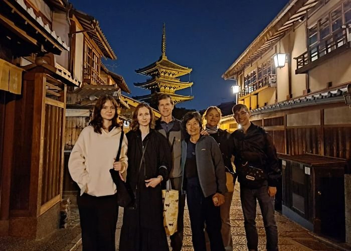 A Kyoto food tour group take a picture on the streets of Kyoto at night, with a pagoda behind them.