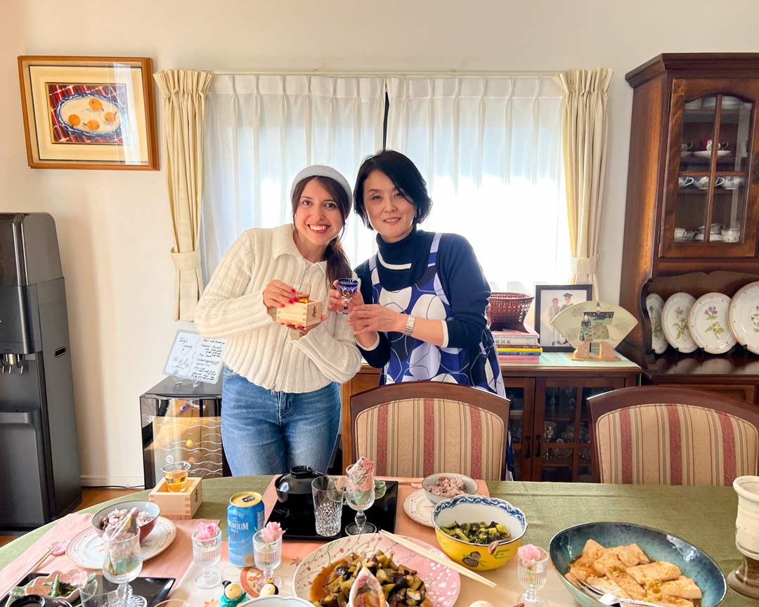 The host and a participant of a Tokyo cooking class holding cups of umeshu in front of a table of vegetarian dishes