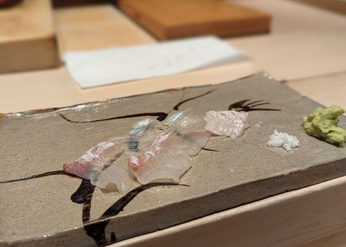 A translucent cut of premium sashimi, served alongside salt and wasabi on a serving tray.