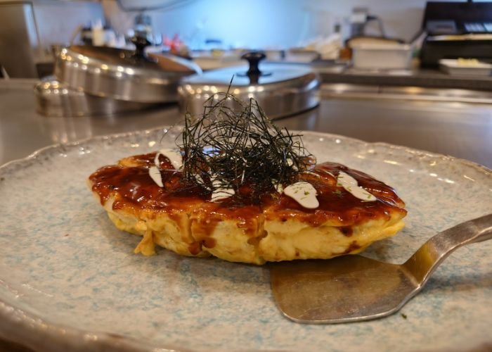 Michelin star okonomiyaki, served on a pottery serving plate with a little okonomiyaki paddle for slicing.