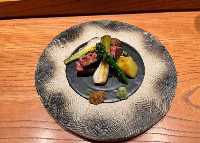 An overhead shot of a dish at a Michelin star tempura restaurant in Osaka, with rare steak, potato, asparagus and spring onion.