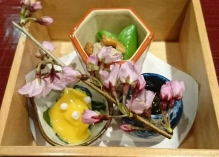 A seasonal selection of dishes served inside a wooden box, with a cherry blossom branch decoration.