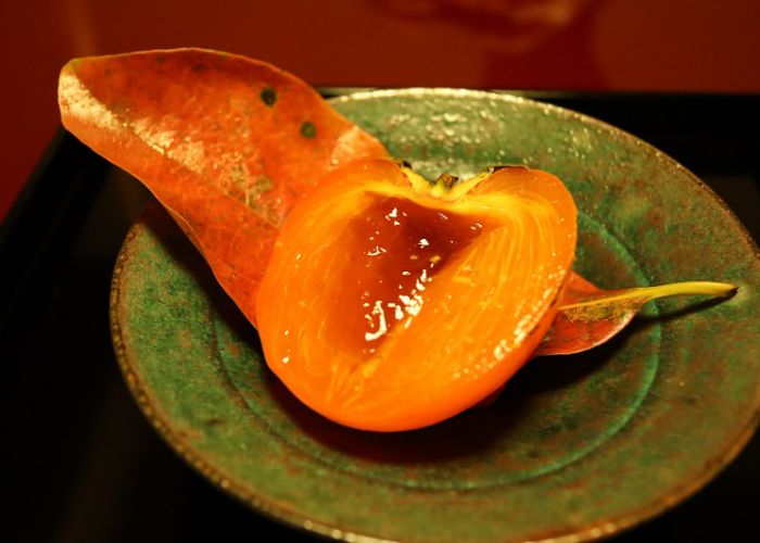 A dessert at Nakamura, a Michelin star restaurant in Kyoto. A persimmon is cut in half and resting on a red-orange leaf.