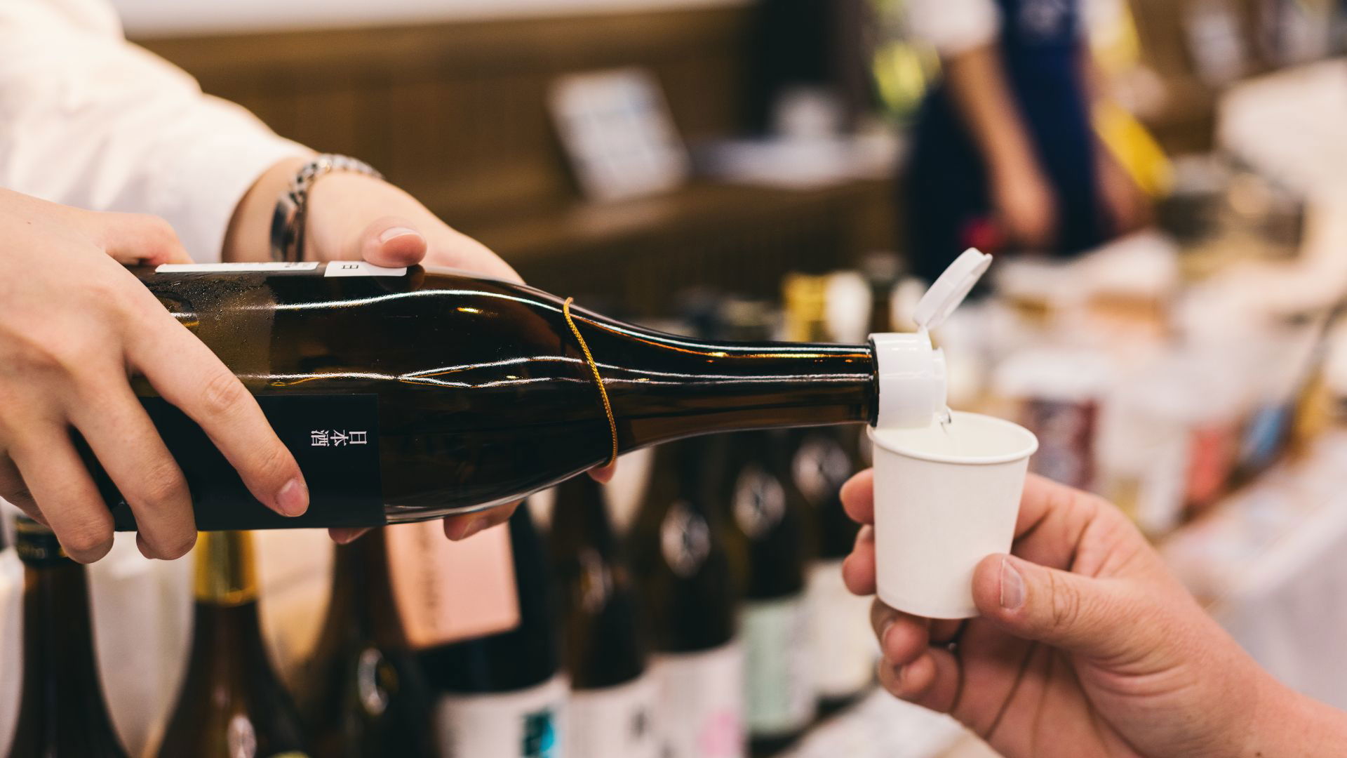 Person pouring sake into cup at a Japanese sake tasting event