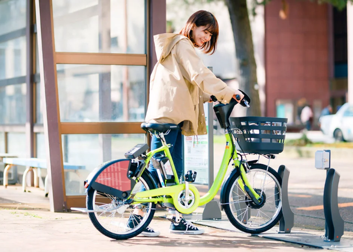 A woman smiles down at a bright green bicycle with a basked, part of Kanazawa's Machi-Nori bike rental scheme.
